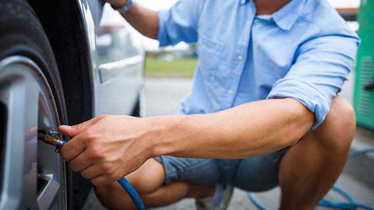 A man in a blue shirt checks his tire pressure.