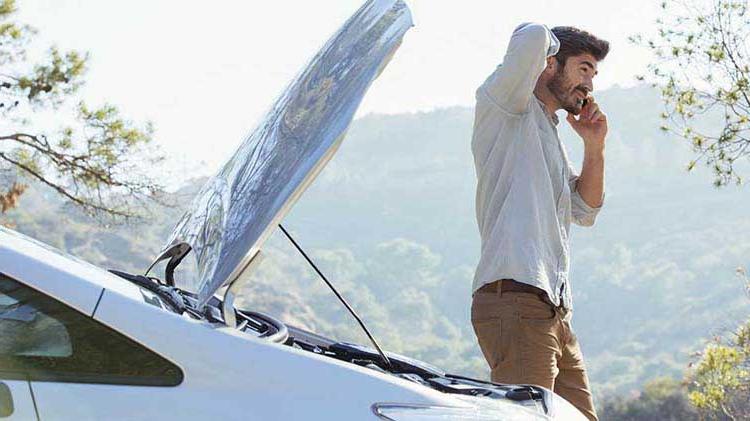 A man talks on his cellphone next to an open car trunk.